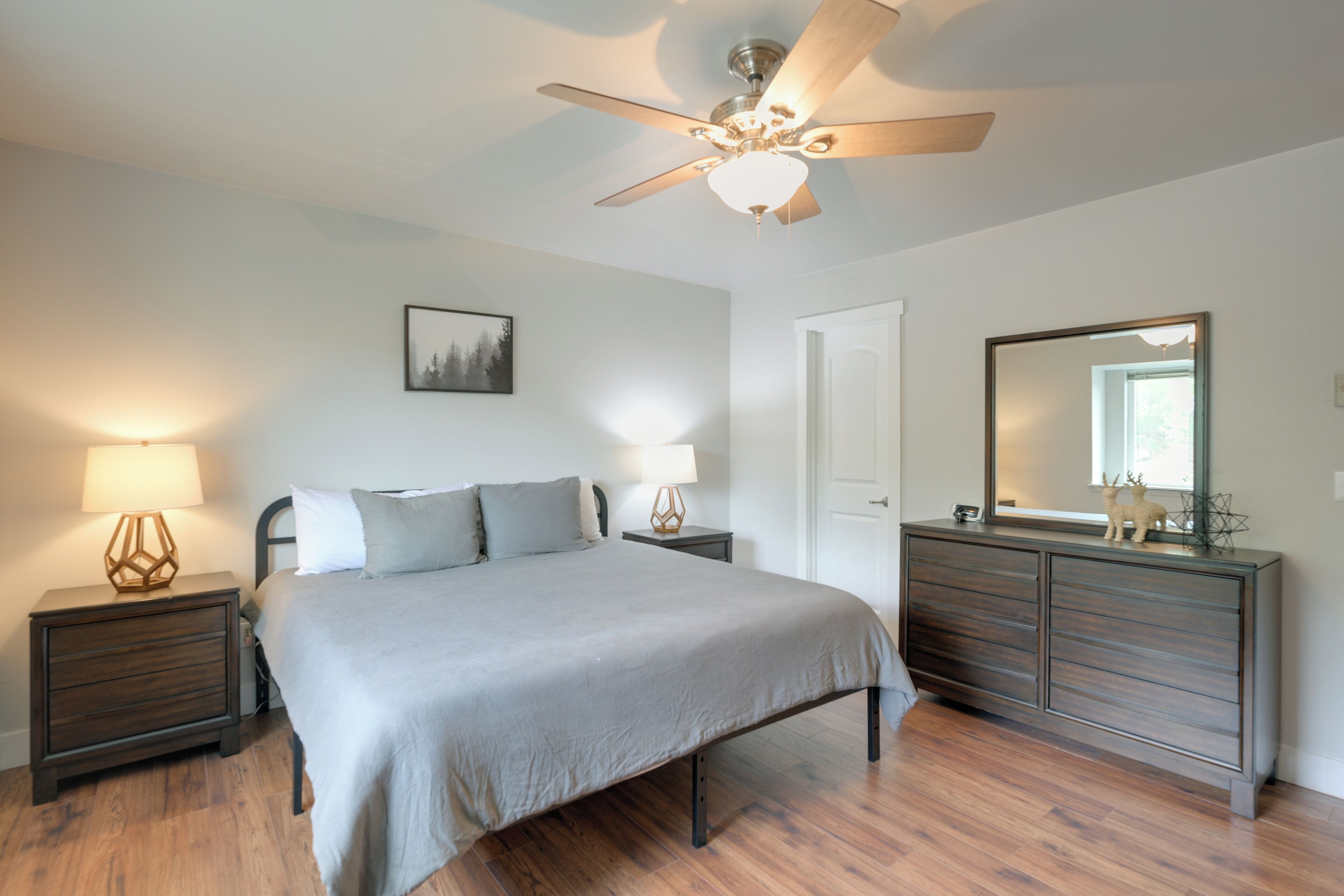 A bedroom with a bed, nightstands, a dresser, a ceiling fan, and a wall-mounted mirror.