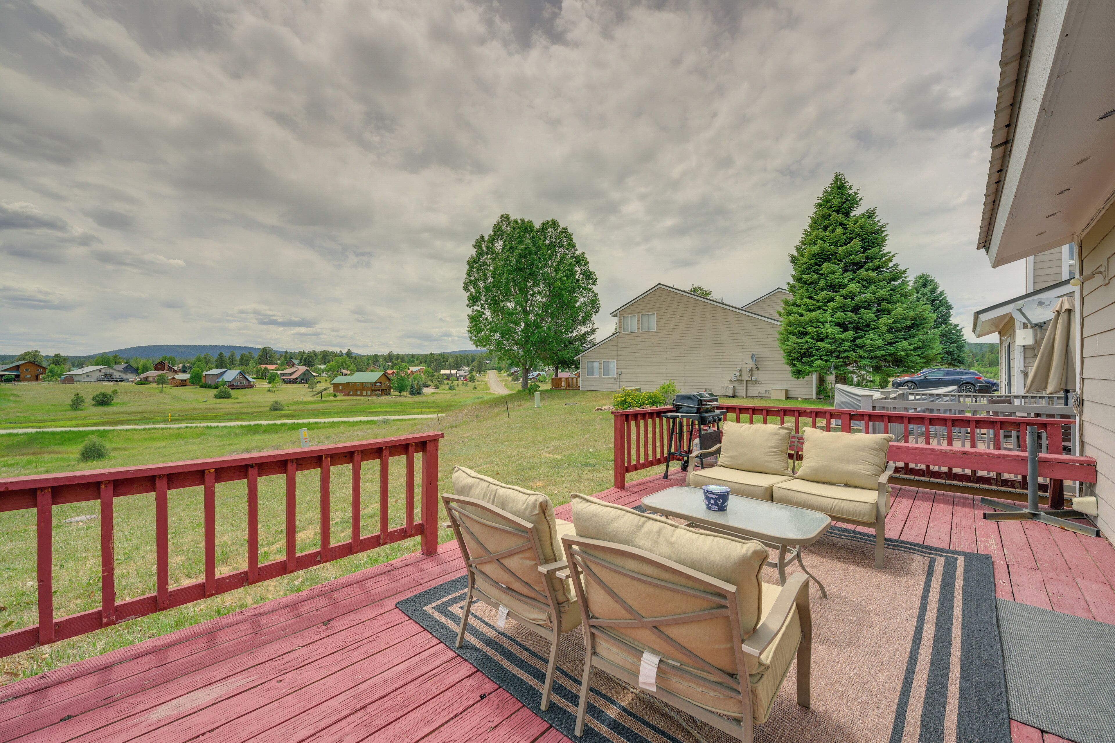 Eine Terrasse mit Gartenmöbeln, Blick auf die umliegende Landschaft und ein Haus im Hintergrund.