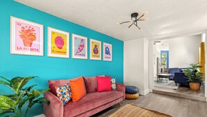 A living room with a teal wall, a red sofa, and four framed posters. - Private Pool! Family Getaway, 5 Mi to Seaworld (San Antonio)