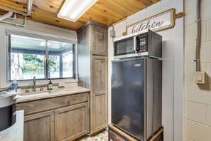 A kitchen with wooden cabinets, a stainless steel refrigerator, a microwave, and a window with a view of greenery.