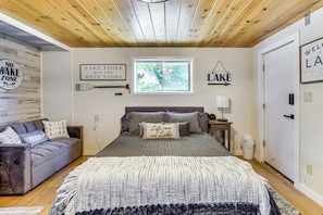 A bedroom with a bed, a nightstand, a lamp, a window, and a wall with a sign saying 'LAKE'.