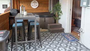 A compact outdoor seating area with a table and chairs, a small step stool, a decorative anchor wall hanging, and a bamboo plant.