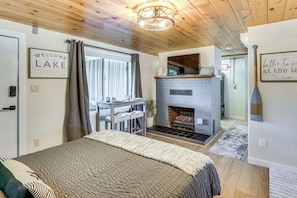 A bedroom with a bed, a fireplace, a dining area, and a view of the lake.
