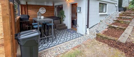 A covered patio area with a table and chairs, a trash bin, and a patterned floor.
