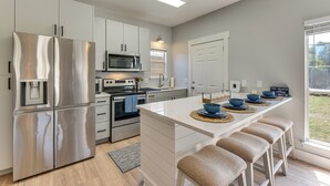 A modern kitchen with stainless steel appliances, a central island with stools, and a view of the outdoors. - Walkable 30A Getaway! Coastal Cottage & Suite (Santa Rosa Beach)