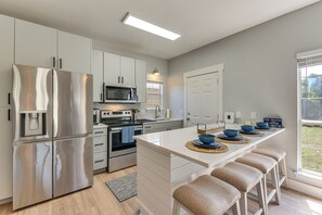 A modern kitchen with stainless steel appliances, a central island with stools, and a view of the outdoors. - Walkable 30A Getaway! Coastal Cottage & Suite (Santa Rosa Beach)
