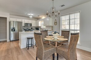 A modern kitchen with a central island, stainless steel appliances, wicker chairs, and a chandelier. - Walkable 30A Getaway! Coastal Cottage & Suite (Santa Rosa Beach)