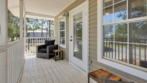 A covered porch with a white railing, a black outdoor chair, and a small table. - Walkable 30A Getaway! Coastal Cottage & Suite (Santa Rosa Beach)