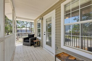 A covered porch with a white railing, a black outdoor chair, and a small table. - Walkable 30A Getaway! Coastal Cottage & Suite (Santa Rosa Beach)