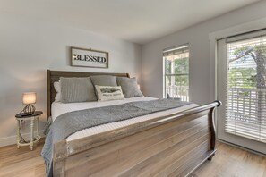 A bedroom with a wooden bed frame, a bedside table with a lamp, a framed sign on the wall, and a window with blinds. - Walkable 30A Getaway! Coastal Cottage & Suite (Santa Rosa Beach)