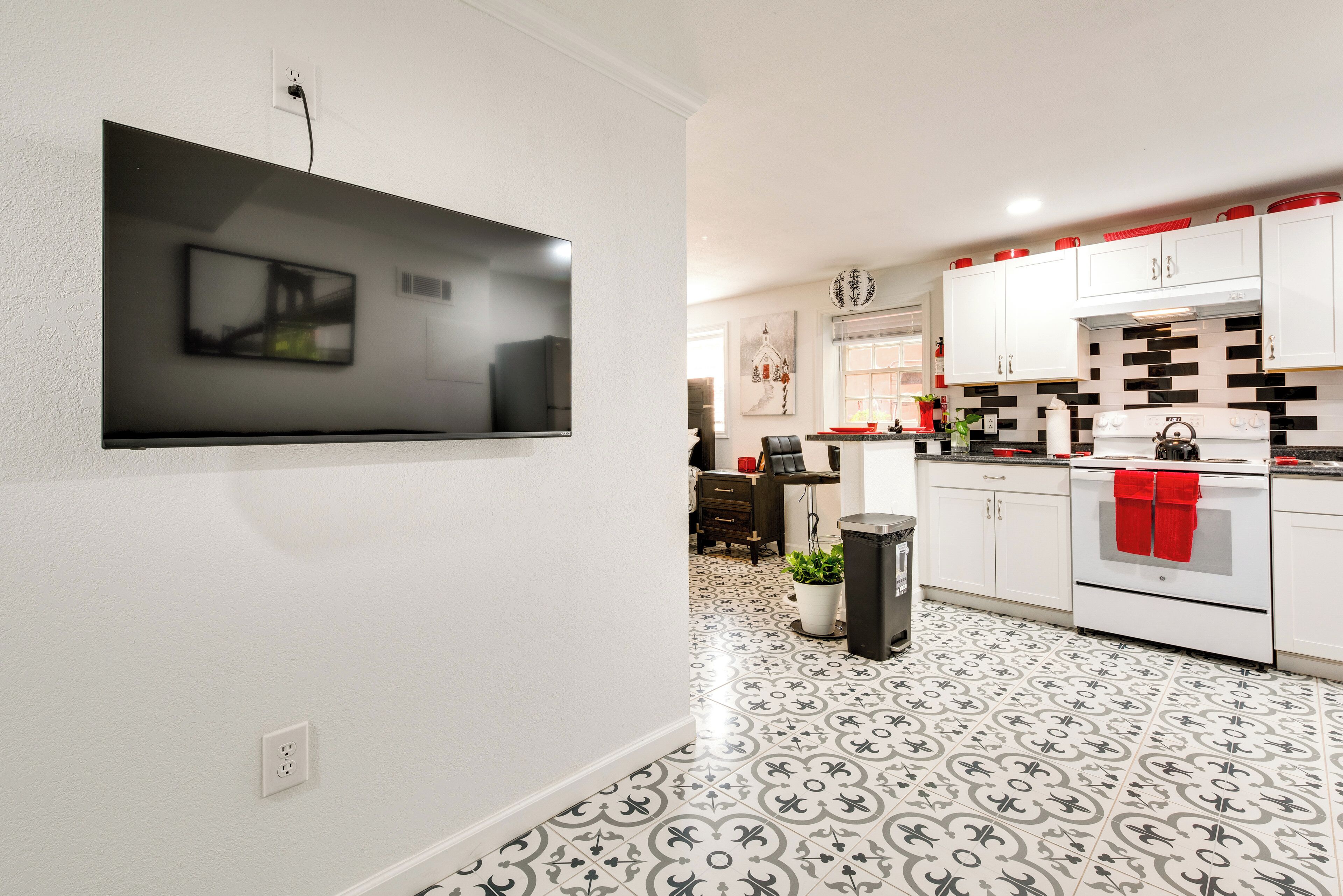 A modern kitchen with white cabinets, a black and white patterned floor, and a TV mounted on the wall.