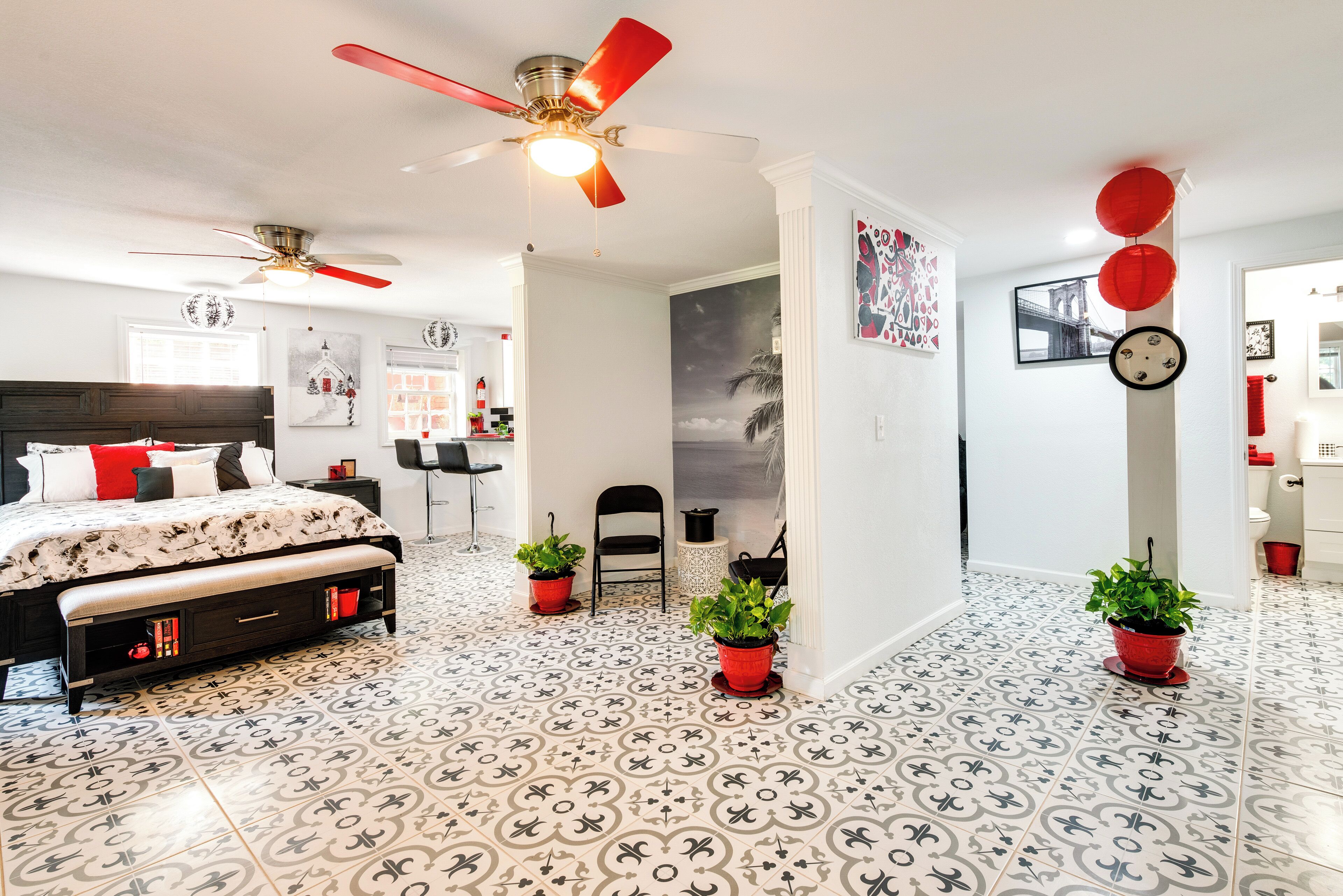 A bedroom with a bed, a ceiling fan, a nightstand, a chair, and a potted plant.