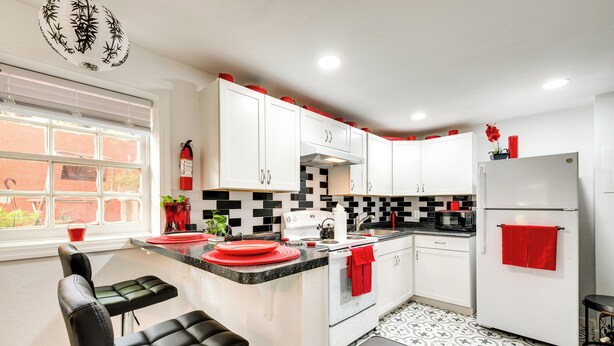 A modern kitchen with white cabinets, a black and white tiled backsplash, a refrigerator with a red towel, and a window with blinds.