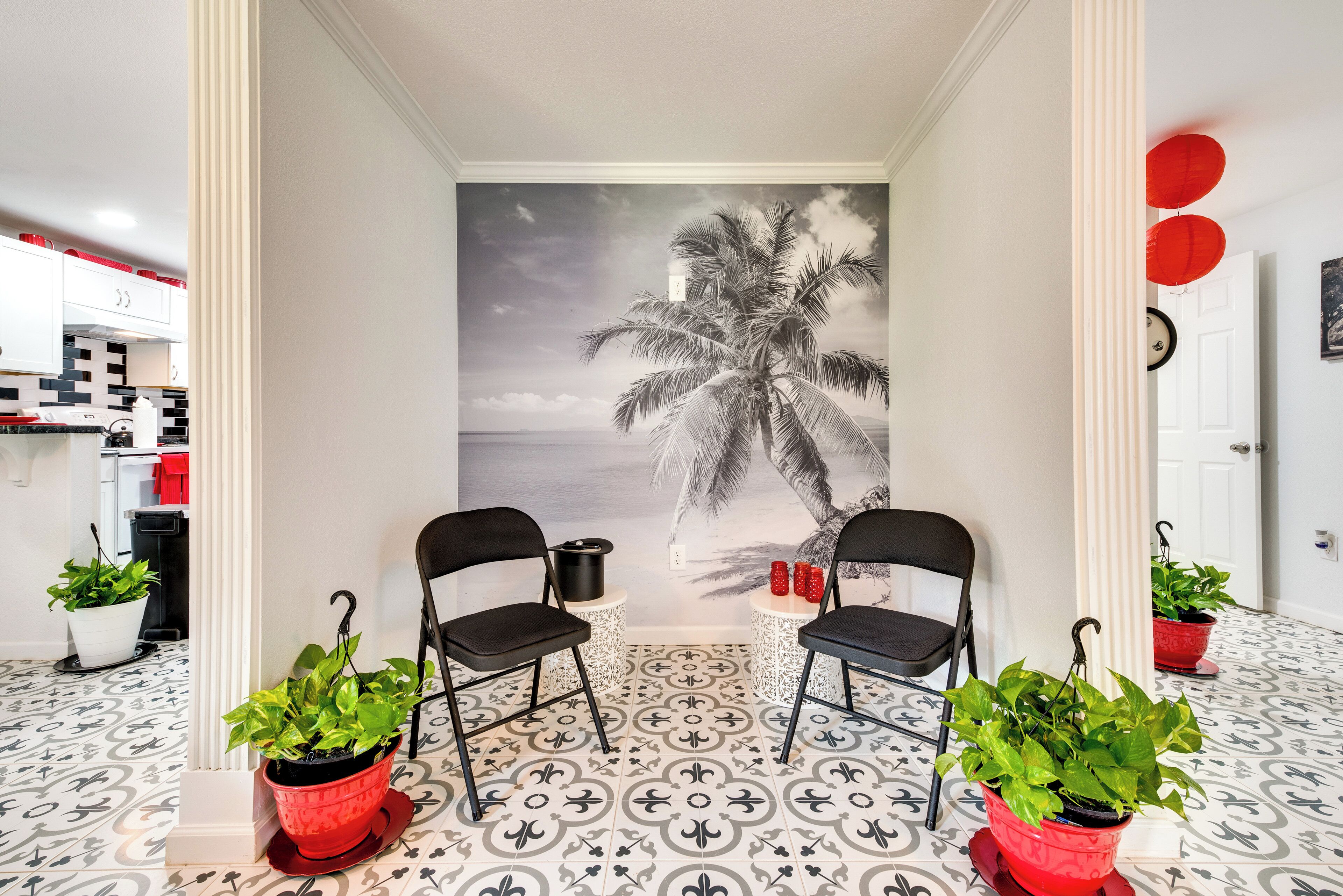 A room with a mural of a palm tree, two black chairs, and potted plants.