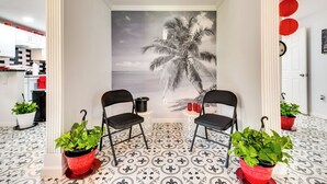 A room with a mural of a palm tree, two black chairs, and potted plants.