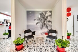 A room with a mural of a palm tree, two black chairs, and potted plants.
