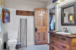 A bathroom with a wooden door, a white toilet, a wooden vanity with a mirror, and a towel rack.