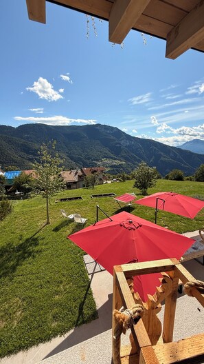 Eine Terrasse mit roten Sonnenschirmen, Blick auf eine gebirgige Landschaft und eine Holzkonstruktion.