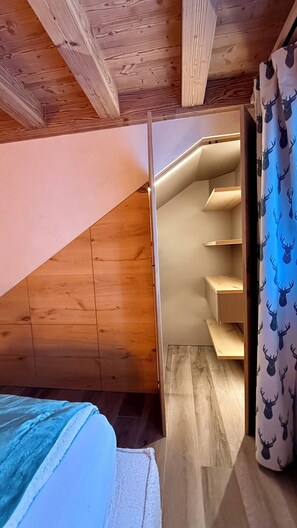 Une chambre avec un plafond en pente, des murs en bois, un lit et un placard intégré avec des étagères.