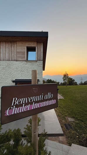 Schild mit der Aufschrift 'Benvenuti allo Chalet Incantato' und Blick auf die Berge im Abendrot.