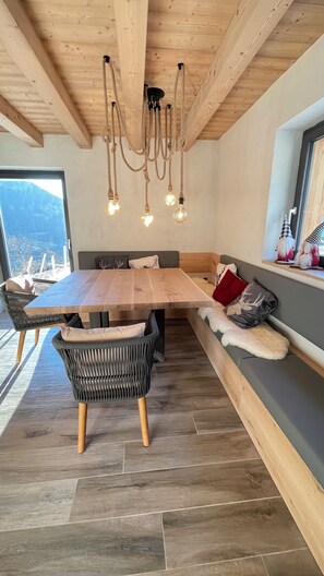 Un coin repas avec une table en bois, des chaises en osier, un banc avec des coussins et un luminaire suspendu.
