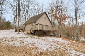 A house with a deck, surrounded by trees and snow on the ground.
