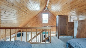 Une pièce avec un plafond en pente, des murs en bois, un lit, une commode et une fenêtre.