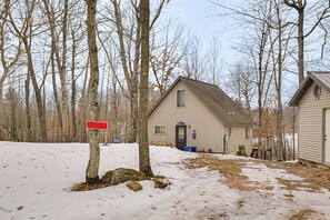 A house with a snow-covered yard, a red sign, and leafless trees.