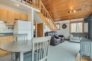 A spacious living area with a dining table, a sofa, a fireplace, and a kitchen with wooden cabinets and a refrigerator.