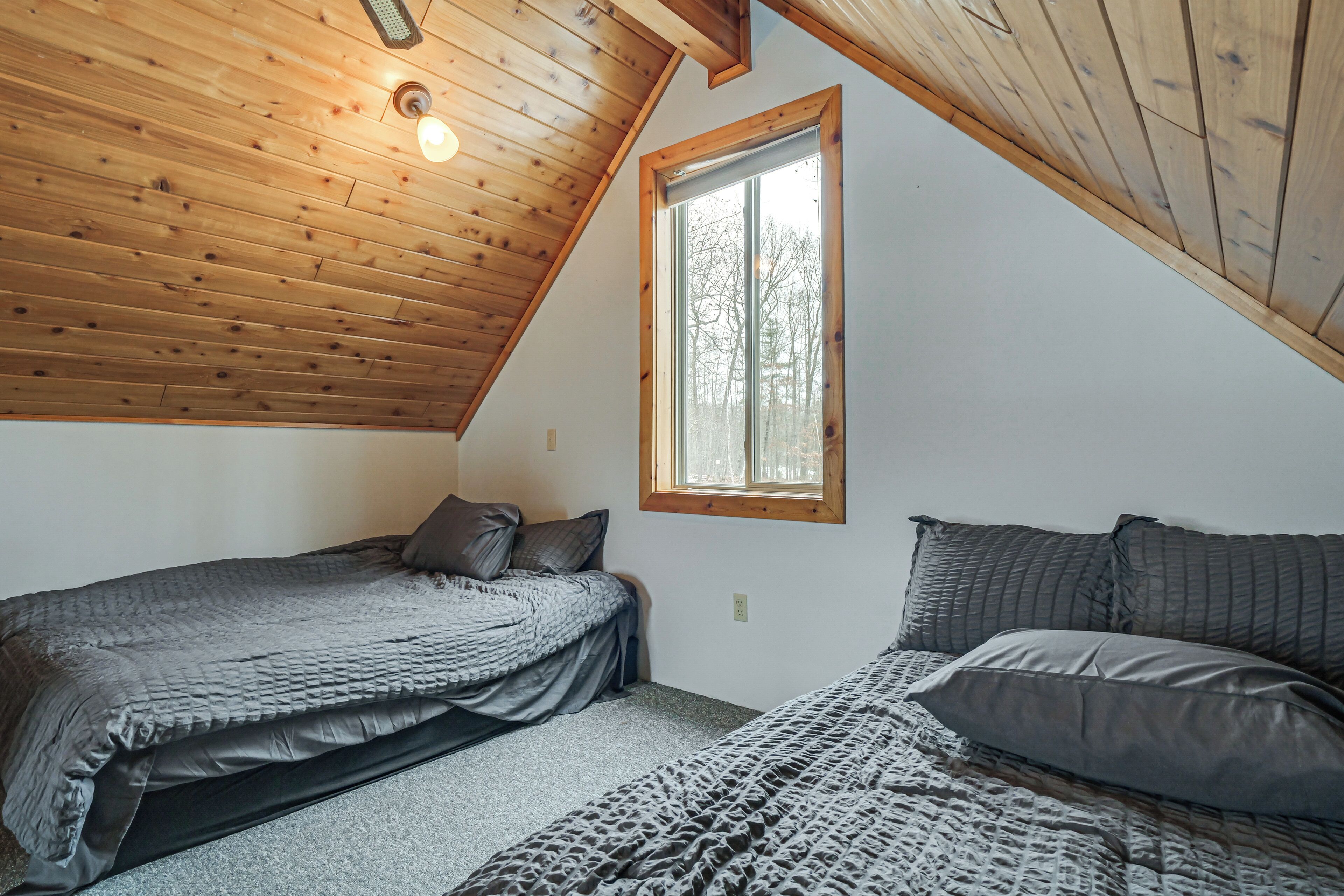 Un dormitorio con dos camas, techo inclinado, una ventana y una lámpara.