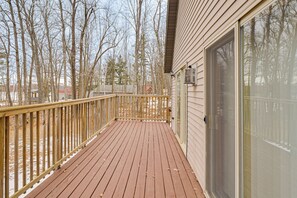 A wooden deck with a glass door and a railing, surrounded by leafless trees.