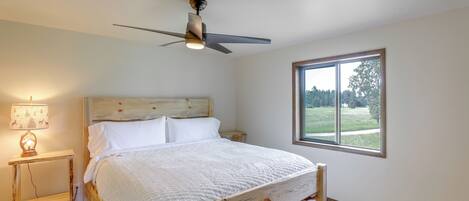 A bedroom with a bed, a ceiling fan, a nightstand with a lamp, and a window with a view of the outdoors.