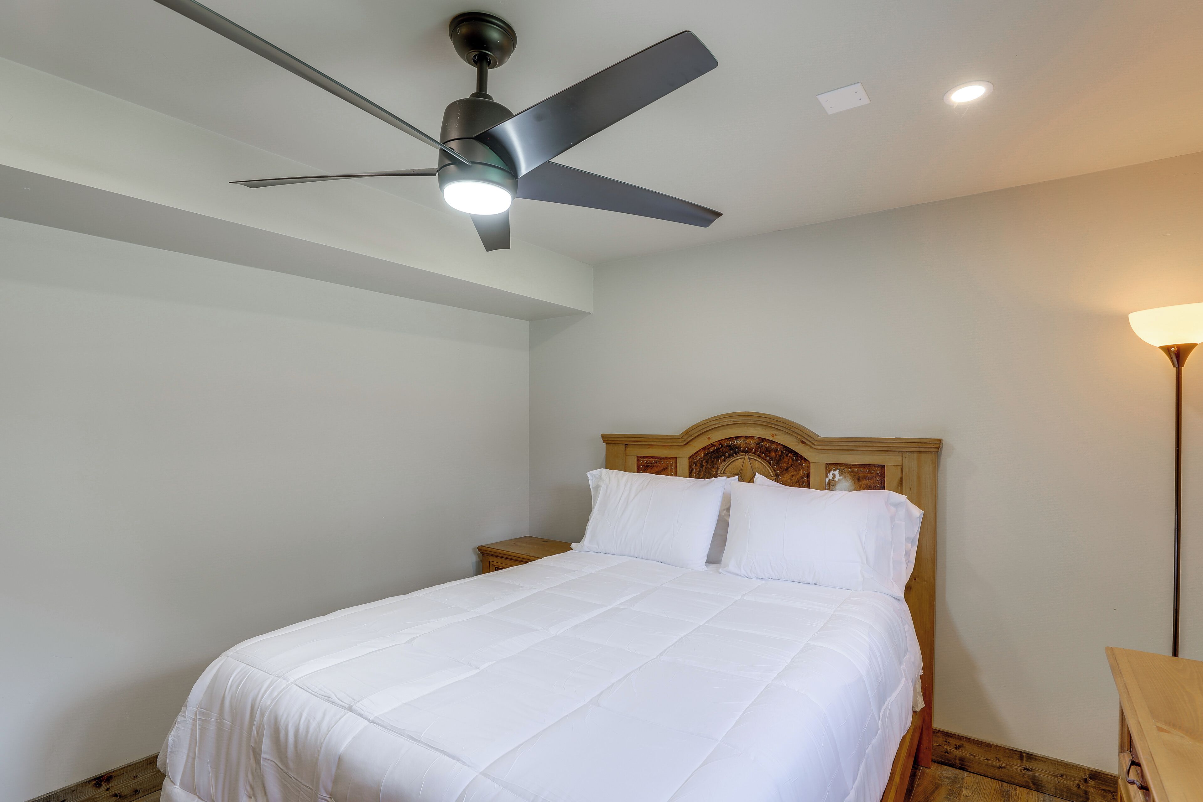 A bedroom with a bed, a wooden headboard, a ceiling fan, a nightstand, and a bedside lamp.