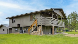 Ein modernes, zweistöckiges Haus mit überdachter Veranda, einer Treppe und einem Holzstapel.