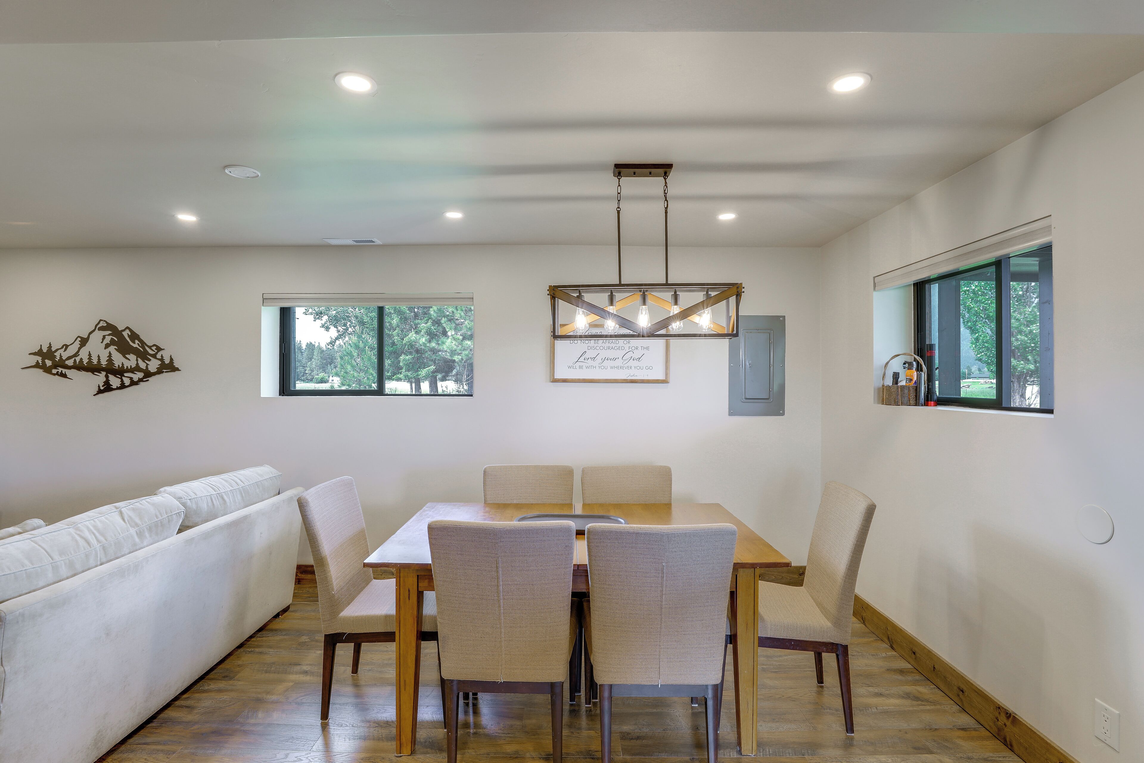 Un comedor con una mesa y sillas de madera, un sofá blanco y una araña.