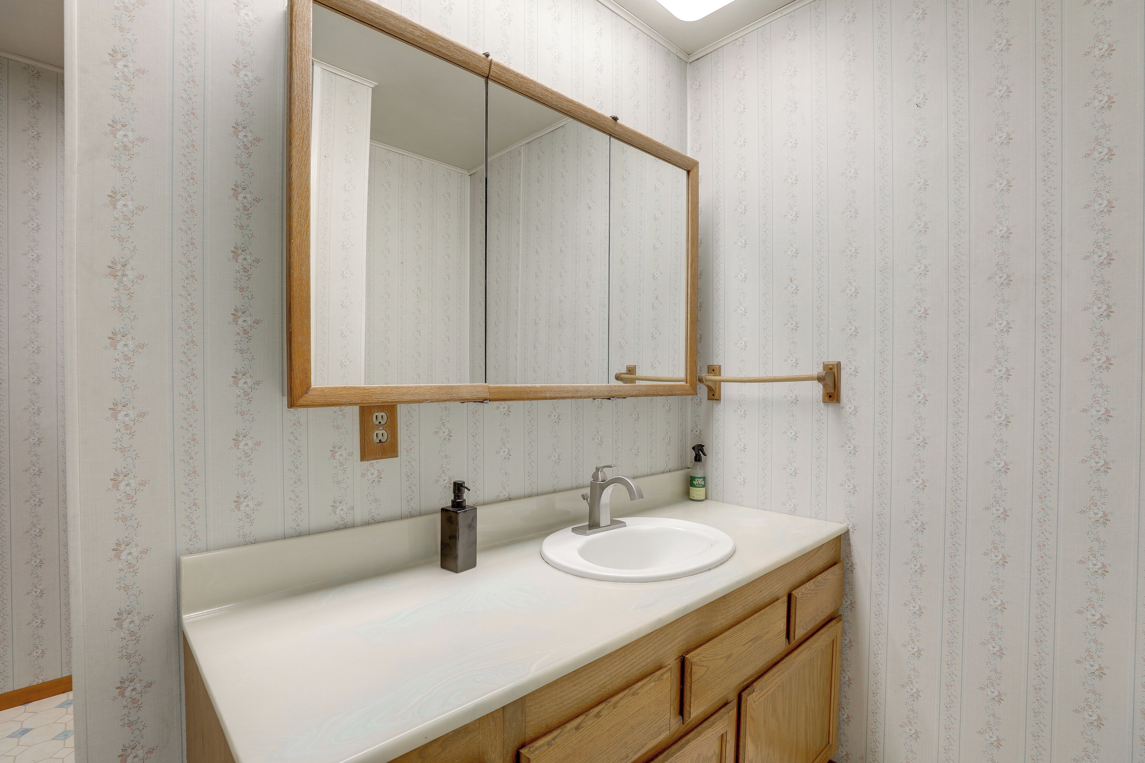 A bathroom with a white sink, wooden vanity, and a large mirror.