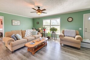 A living room with a beige sofa, a wooden coffee table, a ceiling fan, a potted plant, and a window with blinds.