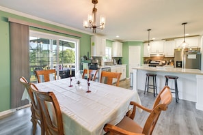 A dining area with a table set for four, wooden chairs, a chandelier, and a kitchen in the background.