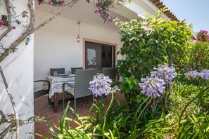 Un patio con mesa y sillas, rodeado de abundante vegetación y plantas en flor.