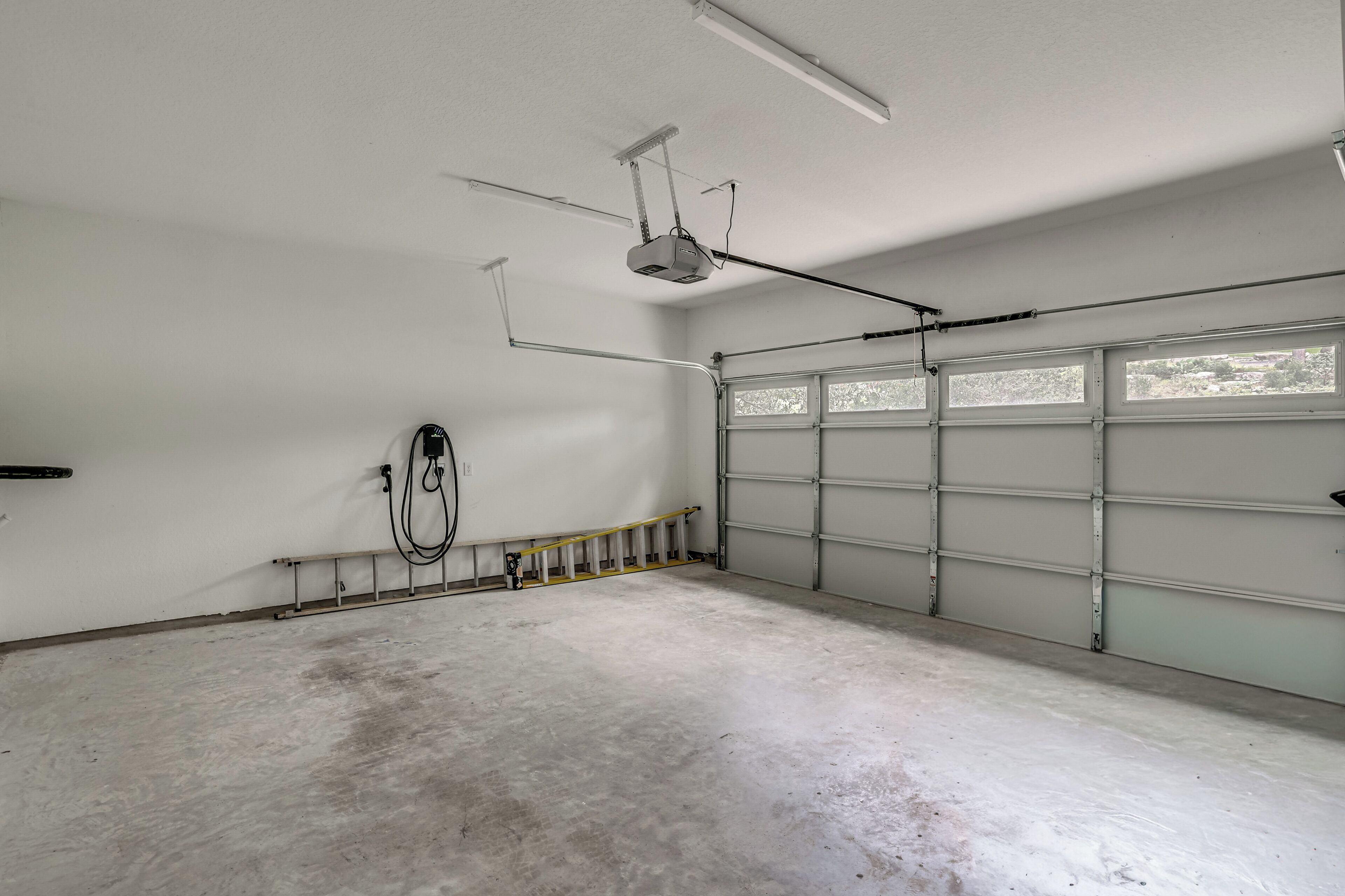 A garage with a ceiling fan, a ladder, and a window with a view of trees.