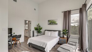 Ein Schlafzimmer mit Bett, Schreibtisch, Stuhl, Sofa und einem Fenster mit Vorhängen.