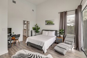 Ein Schlafzimmer mit Bett, Schreibtisch, Stuhl, Sofa und einem Fenster mit Vorhängen.