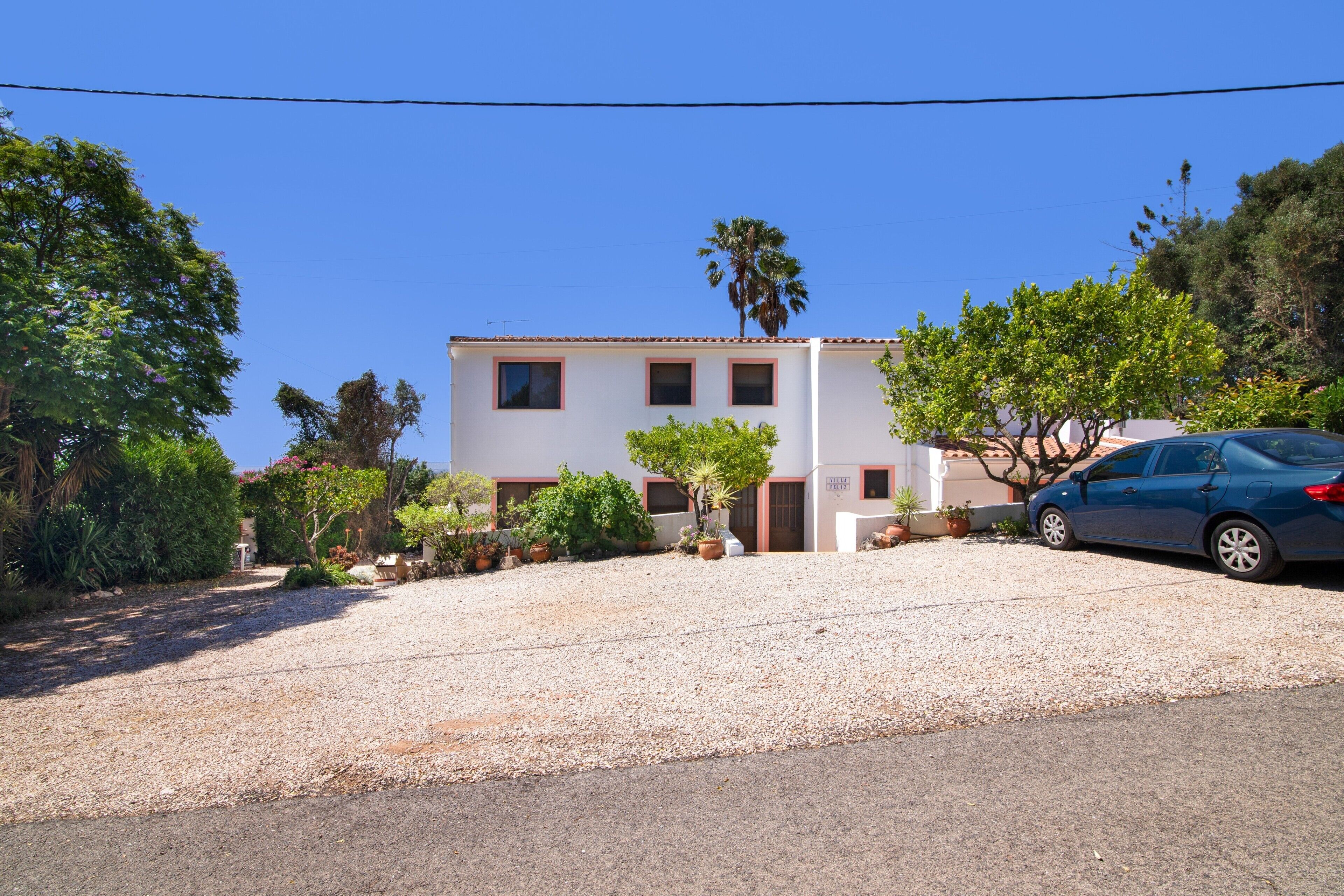A two-story building with a gravel driveway, a parked car, and surrounding greenery.