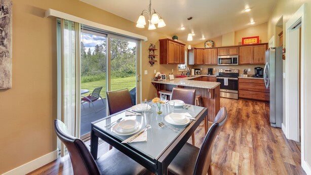 A modern kitchen with wooden cabinets, a dining table set for four, and a large sliding glass door leading to a patio. - 4 Mi to Dtwn! Columbia Falls Home w/ Spacious Yard (Columbia Falls)