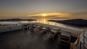 Kattoterassi, jossa on aurinkotuoleja ja upea näköala meren ylle auringonlaskun aikaan.