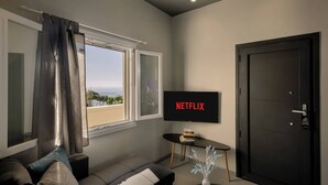 Moderni olohuone, jossa on televisio, jolla näkyy teksti ”NETFLIX”, sohva, pieni pöytä, jossa on kirjoja, ja ovi.