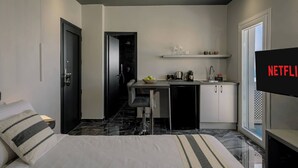 Ein kompaktes Hotelzimmer mit Bett, einer kleinen Küchenzeile, einem Essbereich und einem Fernseher, der das Netflix-Logo zeigt.