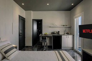 Ein kompaktes Hotelzimmer mit Bett, einer kleinen Küchenzeile, einem Essbereich und einem Fernseher, der das Netflix-Logo zeigt.