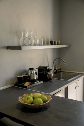 Una cucina con un piano di lavoro, una macchina per il caffè, un bollitore, una ciotola di mele e una dispensa con bicchieri e tazze.