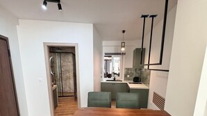 A modern dining area with a wooden table and four green chairs, a kitchen in the background, and a hallway leading to a bathroom. - Athenian Stay 305 Apartment Monastiraki (Athens)